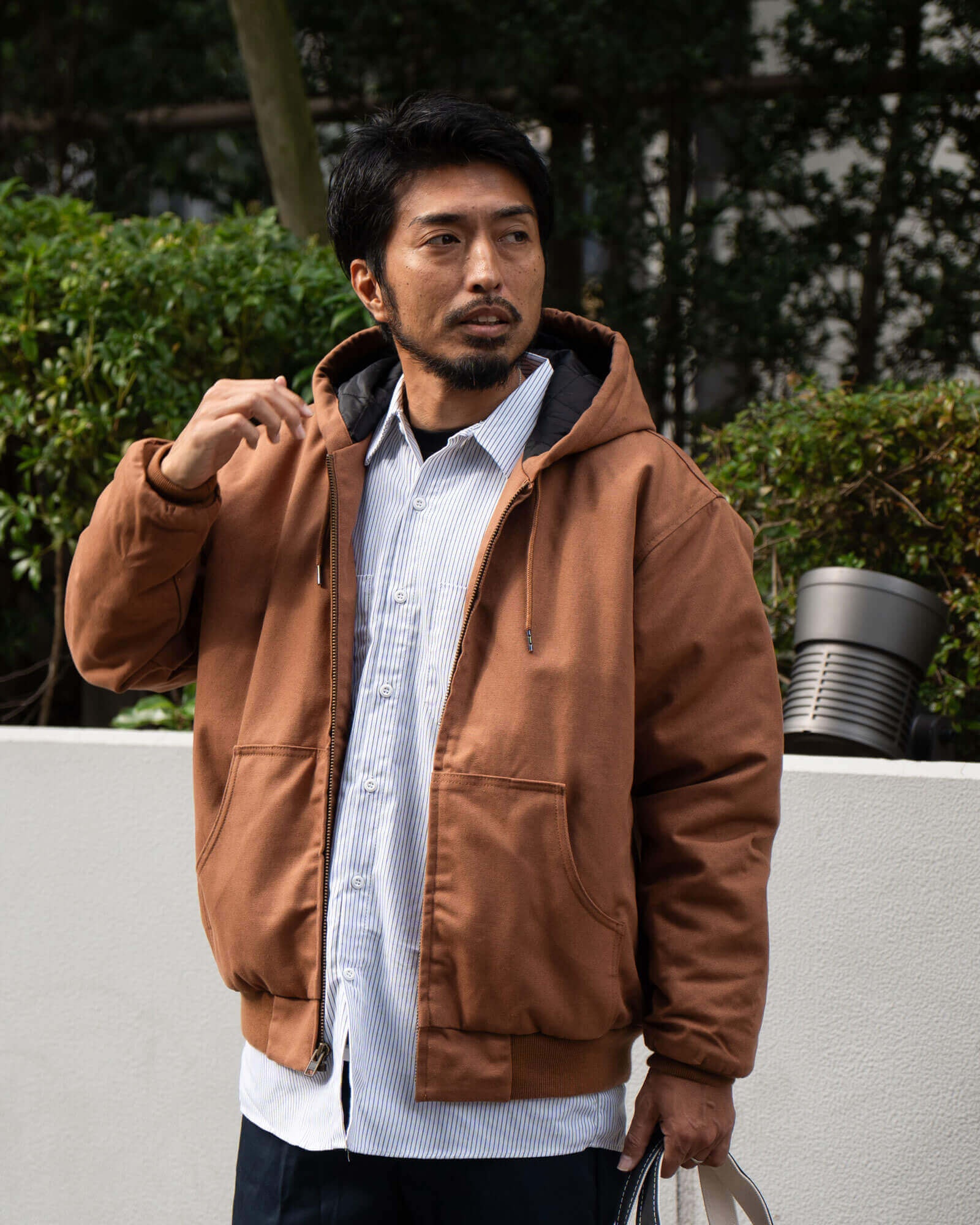 ダックブラウンのフードジャケットとストライプシャツのレイヤード